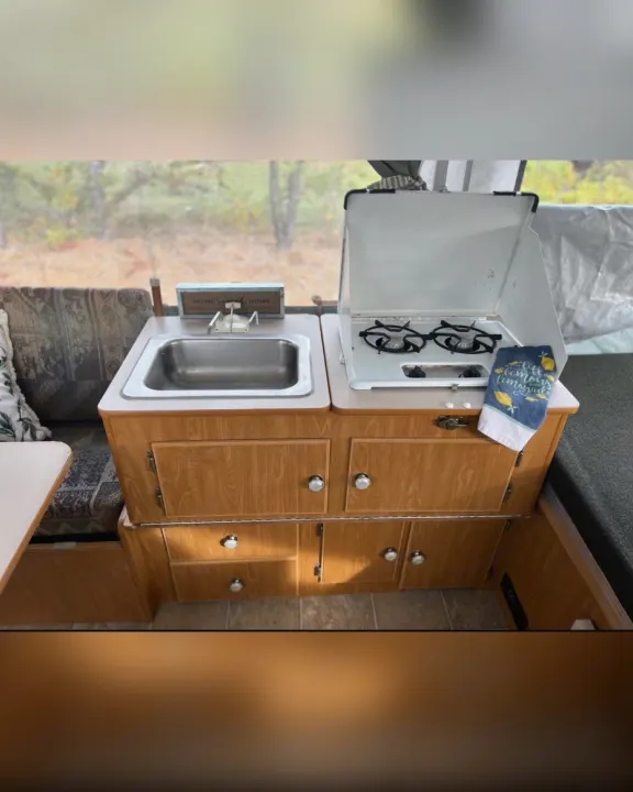 This RV rental features a cozy kitchen with a stainless steel sink, two-burner stove, and wooden cabinetry. Ideal for camping trips.. Fleetwood Other 2005