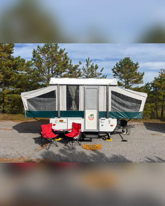 This cozy RV rental pop-up camper is set up at a sunny campsite with red chairs and a fun doormat, perfect for outdoor adventures.. Fleetwood Other 2005