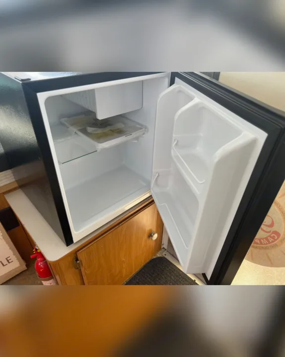 An open, compact black and white mini-fridge in an RV rental, showcasing its small freezer, shelf, and door storage.. Fleetwood Other 2005