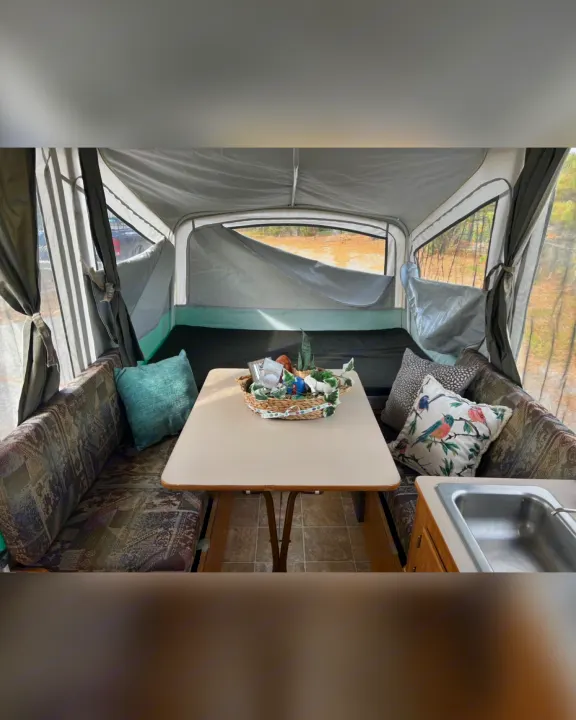 Spacious RV rental interior featuring a bright dining table, patterned benches with pillows, and scenic window views. Includes a sink.. Fleetwood Other 2005
