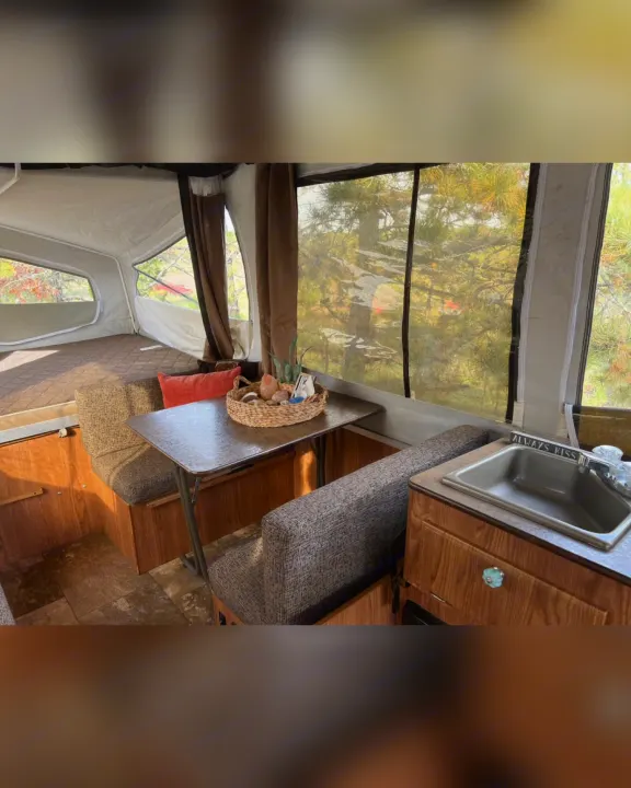 Cozy RV rental interior: bed, dining area with table, and a compact kitchen sink. Enjoy scenic views of trees.. Flagstaff/ForestRiver M.A.C.SeriesM-228 2016