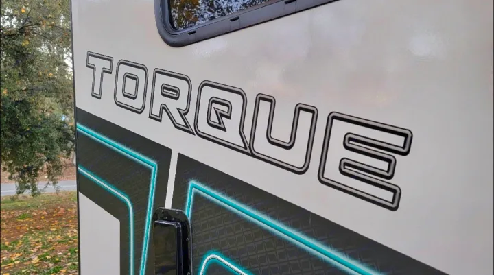Close-up of a 'TORQUE' RV rental side, featuring vibrant teal graphics and a prominent logo.. Heartland Torque 2022