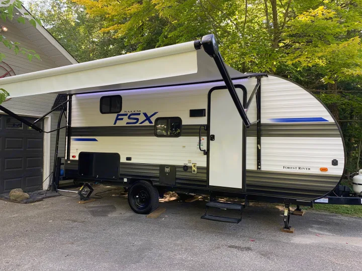 White Forest River Salem FSX RV rental with an extended awning. Parked on asphalt next to a house with trees.. Forest River Salem FSX 2021