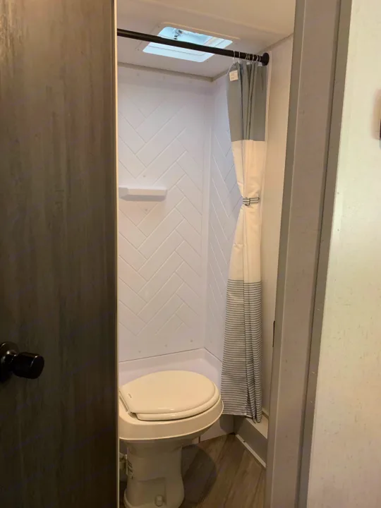Experience a compact RV rental bathroom: white shower with herringbone texture, shower curtain, and toilet.. Forest River Salem FSX 2021