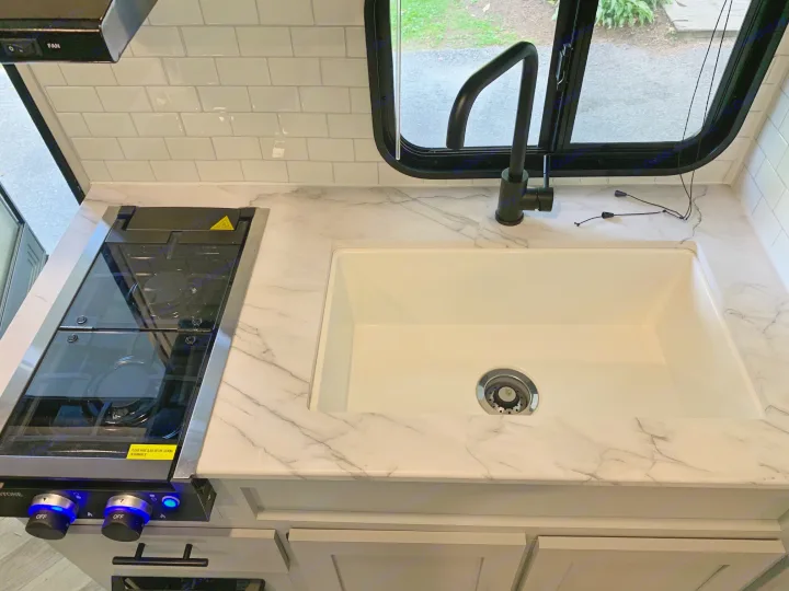 Sleek RV rental kitchen featuring a marble-look counter, white sink, stovetop, and subway tile backsplash. Ready for travel!. Forest River Salem FSX 2021