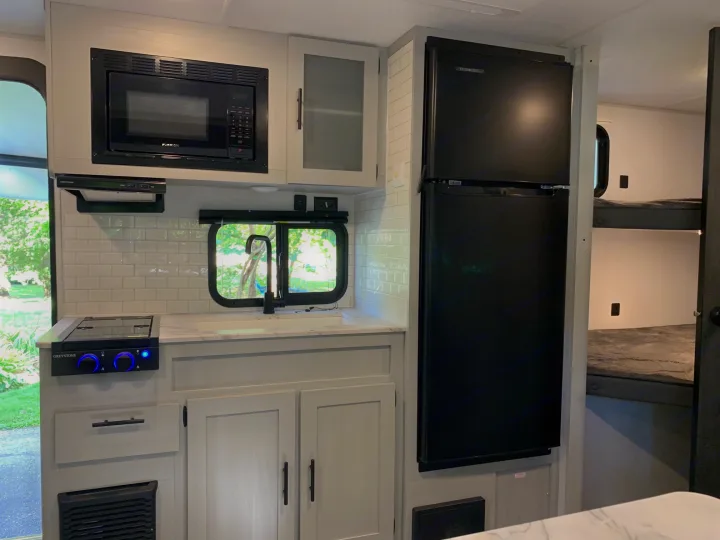 Compact RV rental kitchen with Furrion microwave, Everchill fridge, Greystone stove, and visible bunk beds.. Forest River Salem FSX 2021