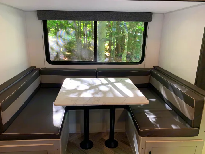 Spacious RV rental dinette featuring U-shaped seating, a marble-look table, and a large window with a forest view.. Forest River Salem FSX 2021