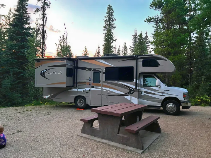 RV rental at a peaceful forest campsite. The motorhome with a slide-out is parked next to a picnic table at dusk.. Thor Four Winds 2014