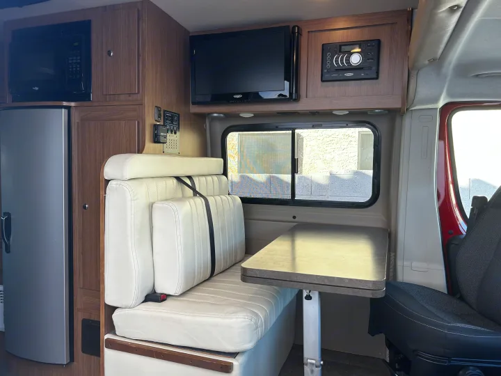 Interior of a compact rv rental showing a microwave, fridge, dinette seating, TV, stereo system, and control panel for comfortable travel.. Winnebago Travato 2015