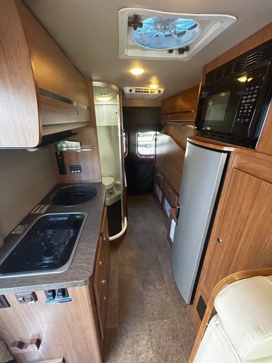 Compact RV rental interior showcasing a well-equipped kitchen, bath, fridge, and microwave. Perfect for road trips.. Winnebago Travato 2015