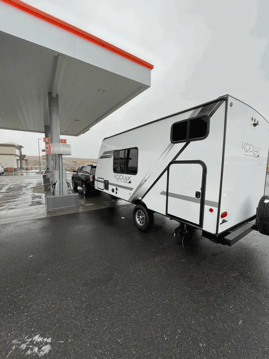 RV rental: Kodiak Cub travel trailer & truck stopped for fuel at a rainy gas station.. Dutchmen Kodiak Cub 175BH 2022