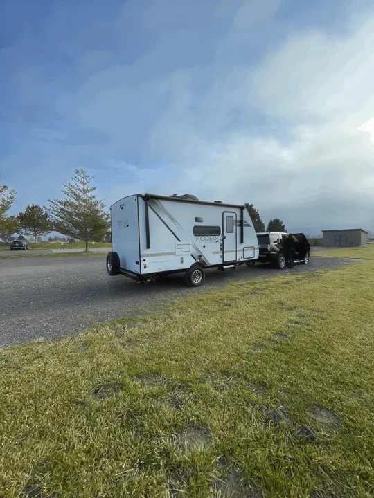 A white Kodiak Cub RV rental hitched to a black SUV on a gravel lot, preparing for travel.. Dutchmen Kodiak Cub 175BH 2022