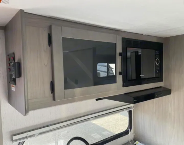RV rental kitchen: Wood grain overhead cabinets, a black microwave, and range hood. A modern RV interior, ready for travel.. Dutchmen Kodiak Cub 175BH 2022