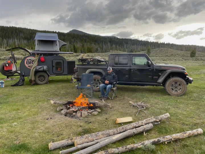 Off-road adventure: Man by campfire with a Jeep & teardrop camper. Explore with an RV rental like this!. BRX Overland trailer 2021