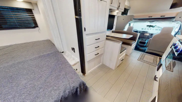 Spacious rv rental interior featuring a cozy bedroom, dinette, and cockpit area with light wood finishes.. Forest River Entrada 2022