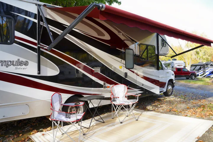 This RV rental, a Class C motorhome, is set up at a fall campsite with an extended awning, chairs, and table.. Itasca Impulse 2013