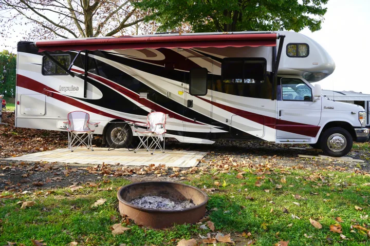 Spacious RV rental parked at a fall campsite with chairs, mat, and fire pit ready for outdoor relaxation.. Itasca Impulse 2013