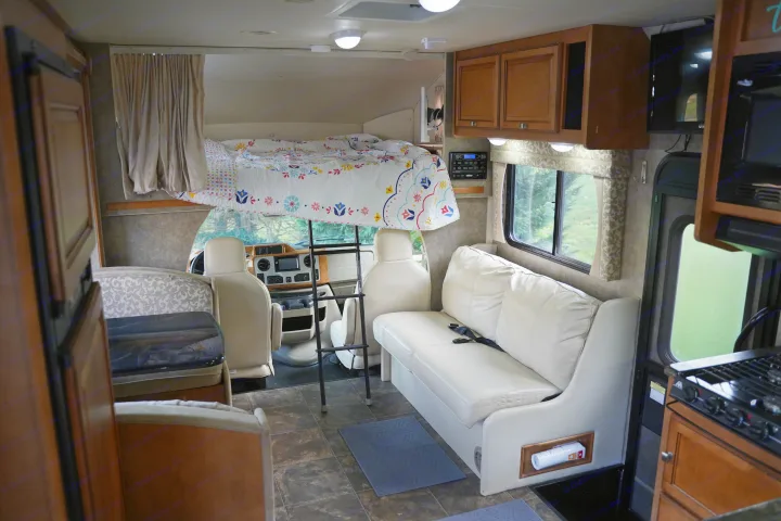 Explore this bright RV rental interior featuring a cozy overhead bed, ample seating, and a functional kitchen.. Itasca Impulse 2013