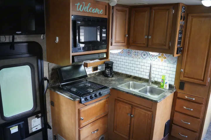 Experience comfortable travel in this RV rental's well-equipped kitchen featuring a microwave, stove, sink, and stylish backsplash.. Itasca Impulse 2013