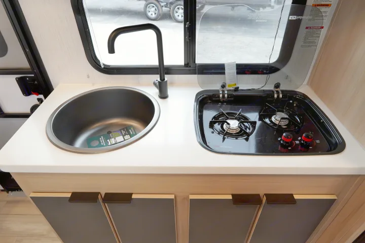 This RV rental's kitchen features a compact design with a dark sink, modern black faucet, and two-burner stove on a light counter.. Cruiser Rv Corp Hitch 2022