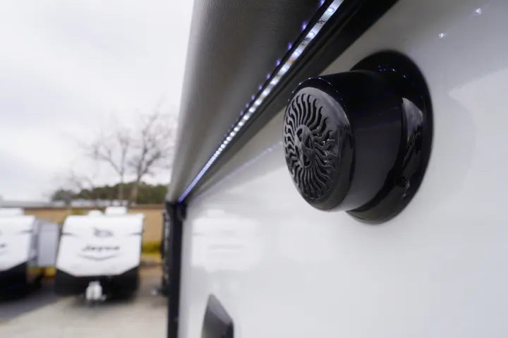 Close-up of an RV rental's white exterior, showing an illuminated awning with LED lights and a mounted outdoor speaker.. Cruiser Rv Corp Hitch 2022