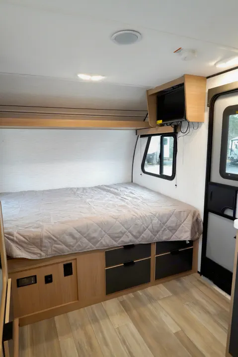 RV rental interior: Comfortable bedroom featuring a bed, mounted TV, storage drawers, and light wood flooring.. Cruiser Rv Corp Hitch 2022