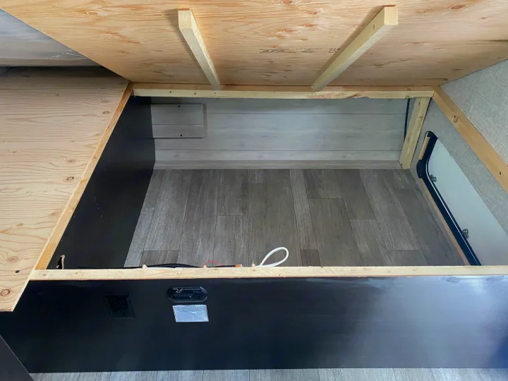 Inside an RV rental: An open under-bed storage compartment with plywood framing, a utility outlet, and a CO/propane alarm.. Jayco Jay Flight SLX STX Edition 2022