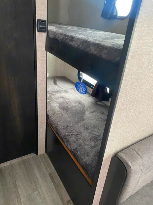 Interior of an RV rental showing cozy bunk beds with gray bedding, a thermostat on the wall, and gray flooring.. Jayco Jay Flight SLX STX Edition 2022
