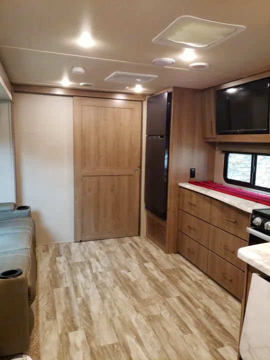 Modern RV rental interior: a well-lit living and kitchen space featuring a sofa, TV, and ample storage cabinets.. Grand Design Imagine XLS 2022