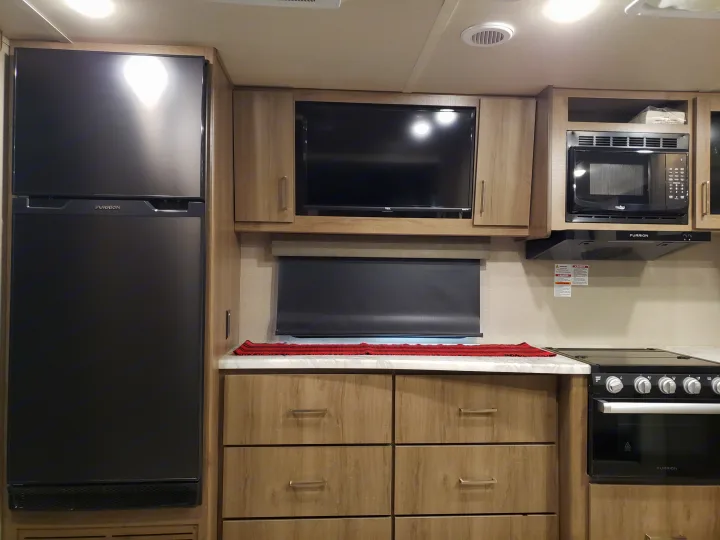 Well-equipped RV rental kitchen: fridge, TV, microwave, and stove within a compact, modern interior.. Grand Design Imagine XLS 2022