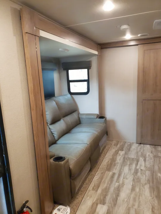 Relax in this RV rental's living area: a plush reclining sofa with cupholders, large window, and stylish wood-look flooring.. Grand Design Imagine XLS 2022