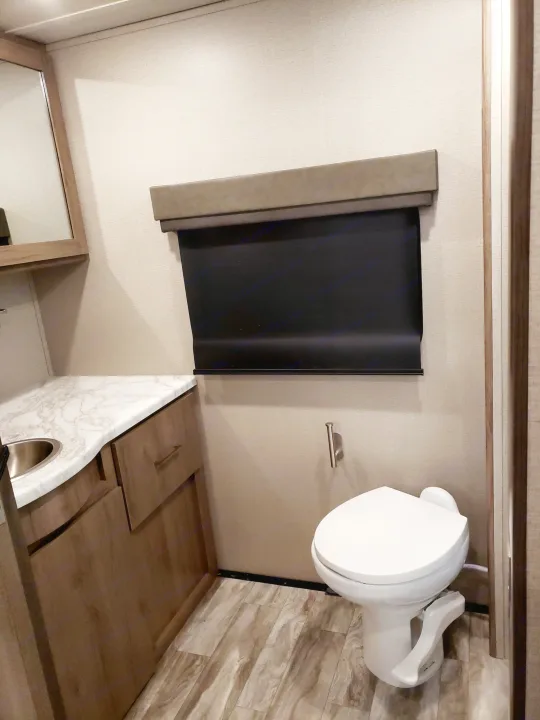 RV rental: well-appointed bathroom with a white toilet, sink, marble counter, wood cabinets, and dark window blind.. Grand Design Imagine XLS 2022
