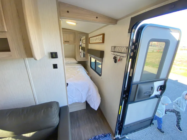 Inside a modern rv rental with a cozy bedroom, sofa, and open door. Kids seen playing outside.. Cruiser RV Shadow Cruiser 2022