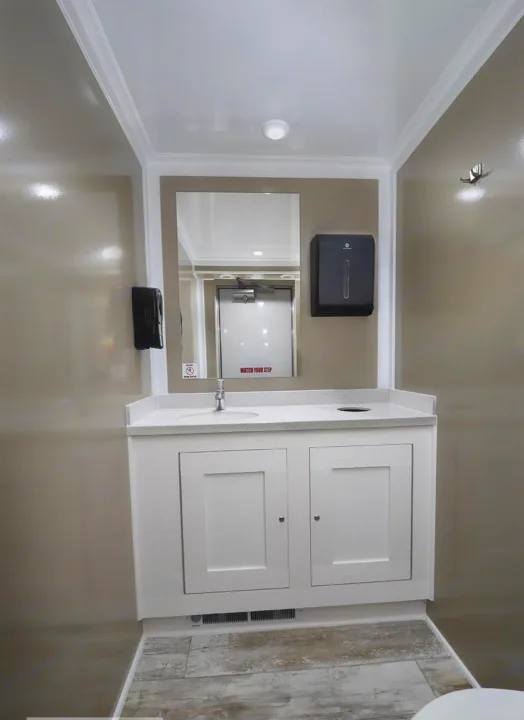 Clean RV rental bathroom featuring a vanity, sink, mirror reflecting a door, and essential dispensers.. Luxury Bathroom 3 Stall 2023