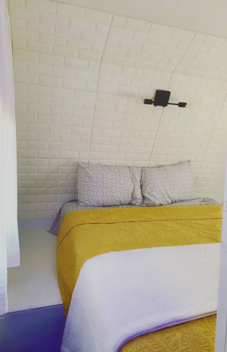 Cozy RV rental bedroom with white brick walls & sloped ceiling. Features a yellow quilt, patterned pillows, and modern light.. Crossroads Zinger 2019