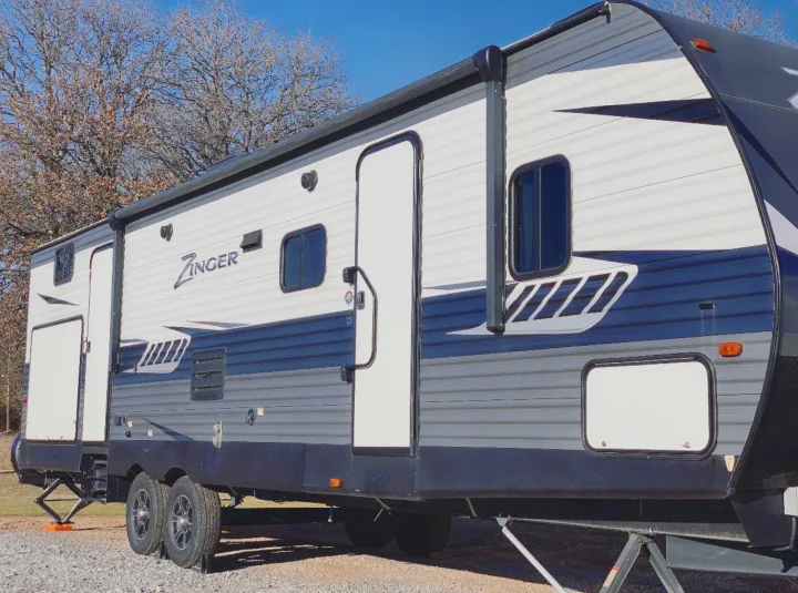 A large Zinger travel trailer RV rental, white, blue, and gray, parked on gravel with an awning, under a clear sky.. Crossroads Zinger 2019