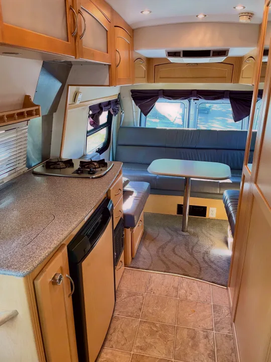 Spacious rv rental interior showing a kitchen with stove, fridge, and a comfortable dinette with bench seating.. Pleasure Way Excel 2007