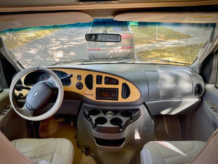 Inside an RV rental: driver's view of the dashboard, Ford steering wheel, and the road ahead through the windshield, showing a car.. Pleasure Way Excel 2007