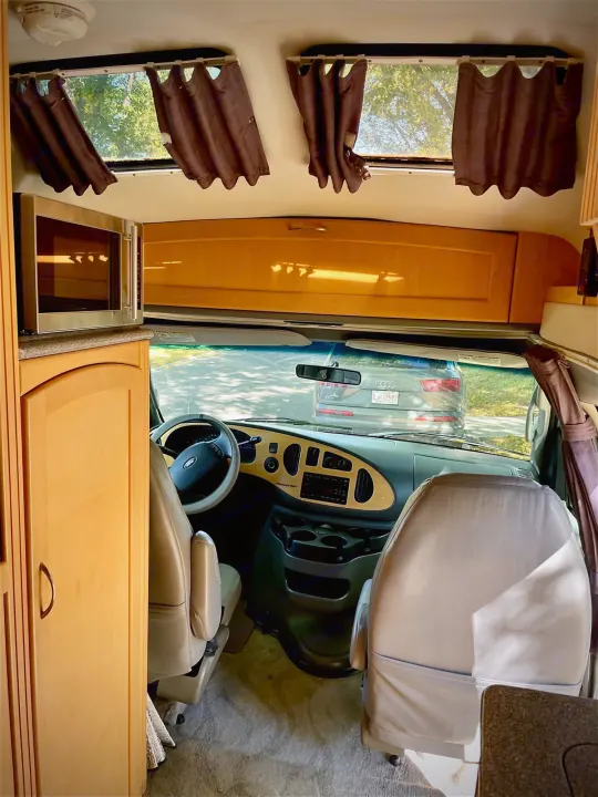 Inside this rv rental, looking from the living area towards the driver's cockpit, with microwave, wood cabinetry, and passenger seats.. Pleasure Way Excel 2007