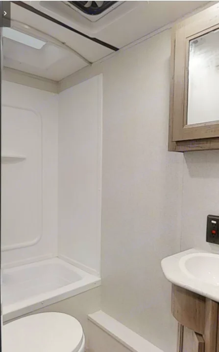 This RV rental bathroom offers essential amenities: a white tub/shower, toilet, and a vanity with sink and mirror.. Keystone Hideout 21BHWE 2021