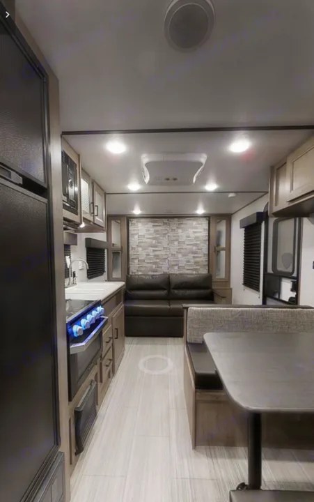 This modern RV rental interior features a functional kitchen, comfy sofa, and dinette. Note the stone accent wall.. Keystone Hideout 21BHWE 2021