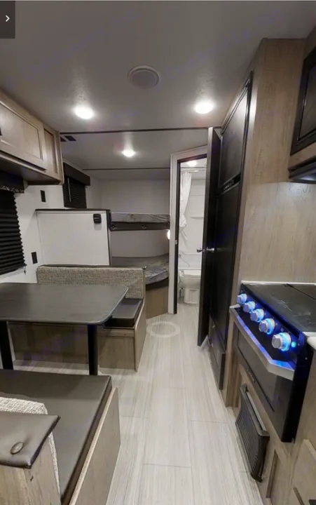 Inside an RV rental: full kitchen with stove, dinette, bunk beds, and bathroom. Bright interior, ready for travel.. Keystone Hideout 21BHWE 2021