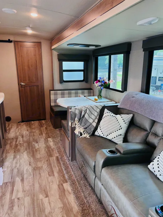 This RV rental shows a cozy living area with a grey sofa, patterned pillows, a dining booth, and wood-look flooring.. Grand Design Imagine 2022
