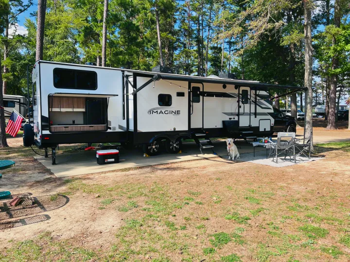 Spacious Imagine RV rental parked at a serene campground with outdoor amenities and a friendly dog.. Grand Design Imagine 2022