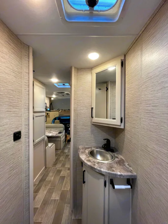 RV rental interior: A bright bathroom with sink and mirror, providing a glimpse of the dinette and front cab.. Thor Chateau 2022