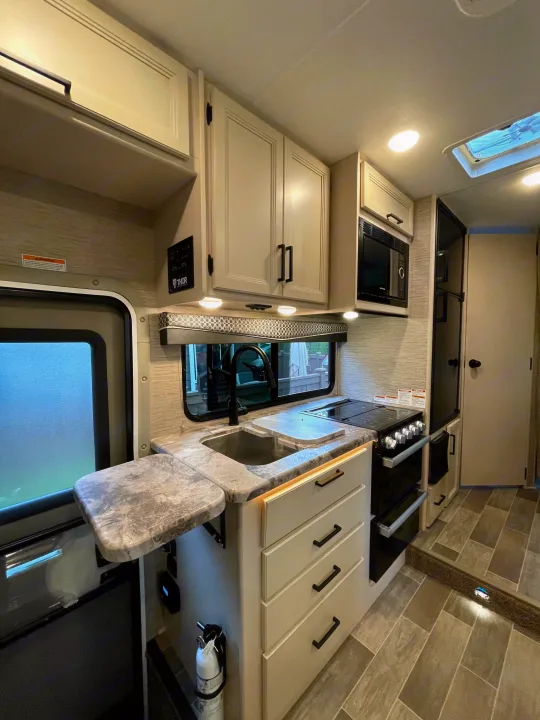 Explore this modern rv rental's kitchen: a full galley with sink, stove, microwave, light cabinetry, and bright lighting.. Thor Chateau 2022