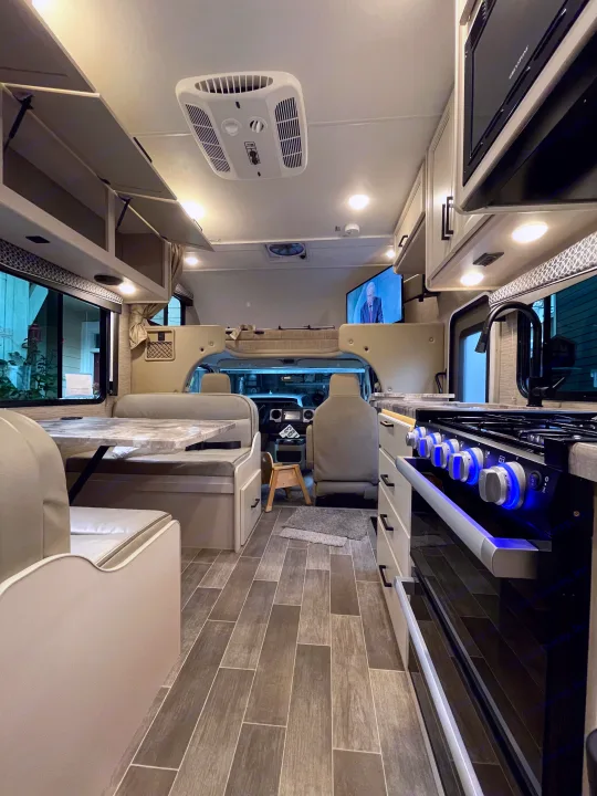 Spacious and modern RV rental interior featuring a kitchen with blue-lit stove, comfortable seating, and wood-look flooring.. Thor Chateau 2022
