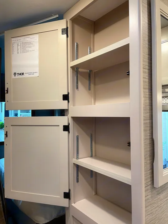 Inside an RV rental: open overhead cabinets reveal adjustable shelves for storage. A Thor Motor Coach data card is visible.. Thor Chateau 2022