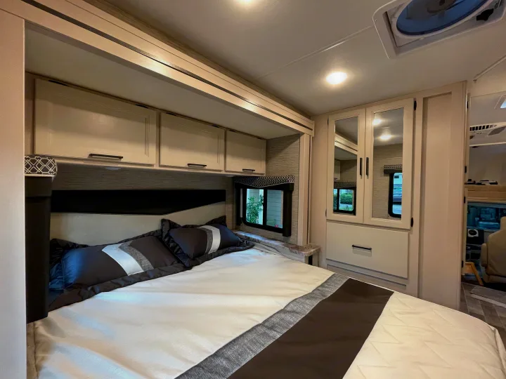 Modern RV rental bedroom: a bed with patterned bedding, overhead cabinets, and mirrored closet. Cozy travel.. Thor Chateau 2022