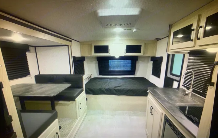 Spacious RV rental interior featuring a cozy bed, a dinette to the left, and a compact kitchen on the right.. Coachmen Apex Nano 2021